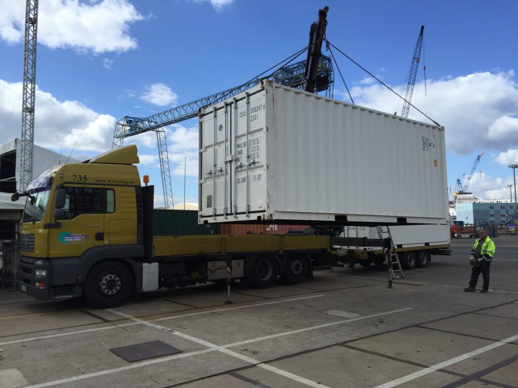 Lkw mit Ladekran setzt einen 20-Fuß-Container neben dem Fahrzeug ab