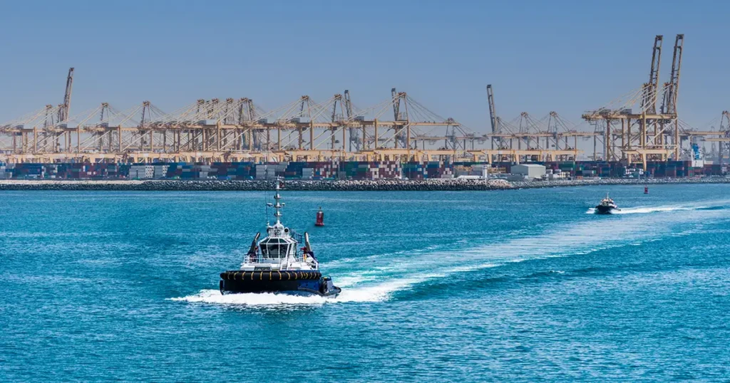 Schlepperboot vor dem Containerhafen Jebel Ali in den Vereinigten Arabischen Emiraten mit zahlreichen Kränen und Containern im Hintergrund