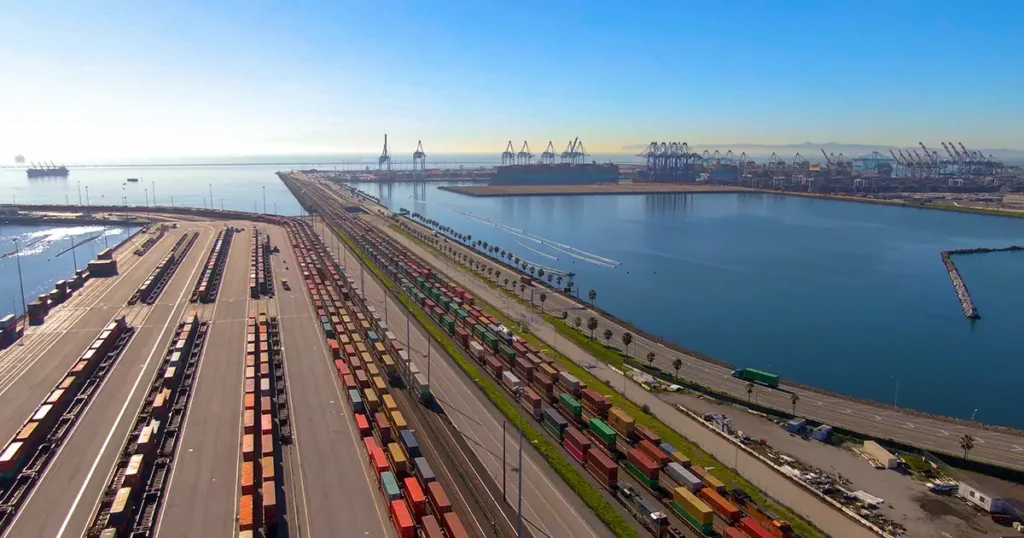Luftaufnahme des Port of Los Angeles mit Containerterminals, Kränen und gestapelten Schiffscontainern entlang der belebten Industrieeisenbahn