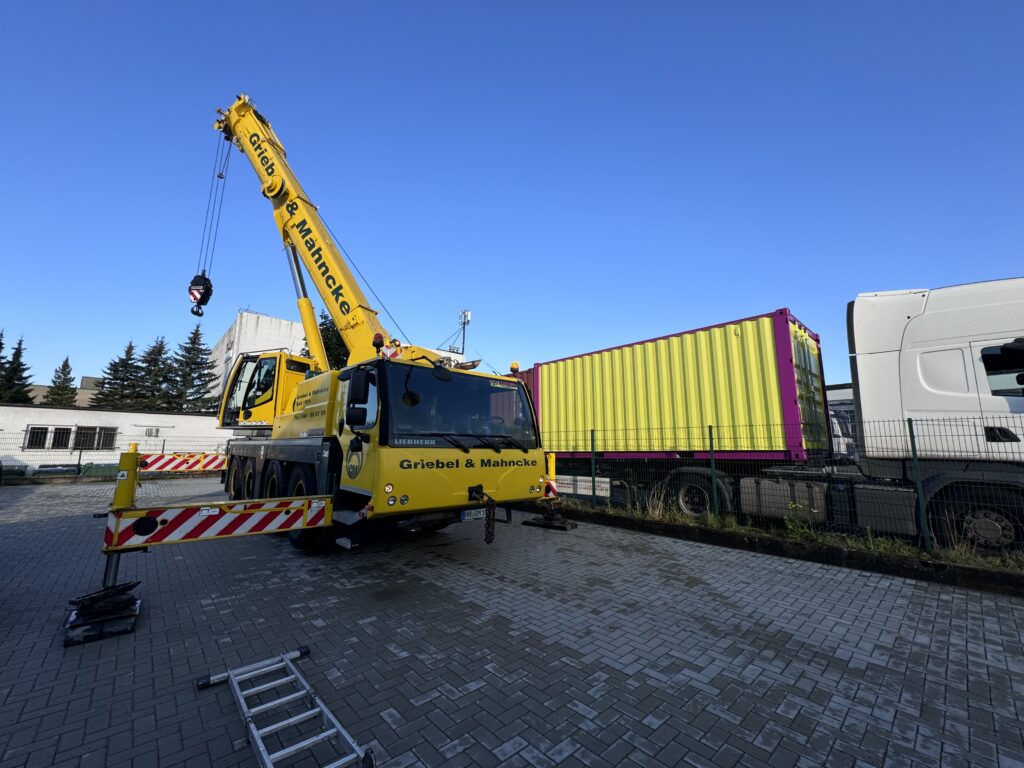 Mobilkran kurz davor einen Container über einen Zaun auf eine Freifläche zu haben