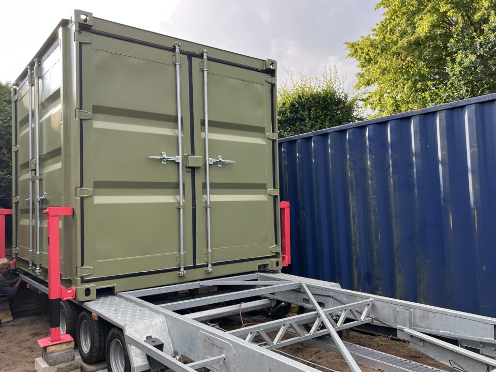 Container-Trailer mit vier eingehängten Containerstützen, der Container ist hochgekurbelt und der Anhänger fährt heraus
